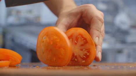 Closeup-of-a-woman-cutting-and-chopping-tomato-by-knife-on-wooden-board